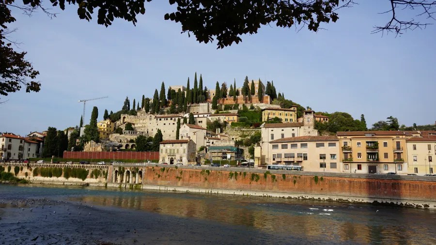 Historic buildings and a castle on a tree-covered hillside overlooking a river.