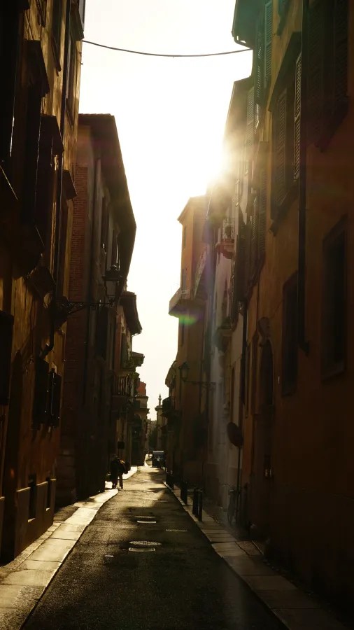 A narrow European alleyway with sunlight streaming between tall historic buildings