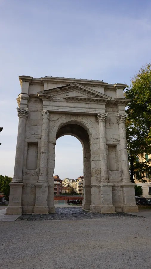 Ancient stone triumphal arch with fluted columns and a pediment against a clear sky