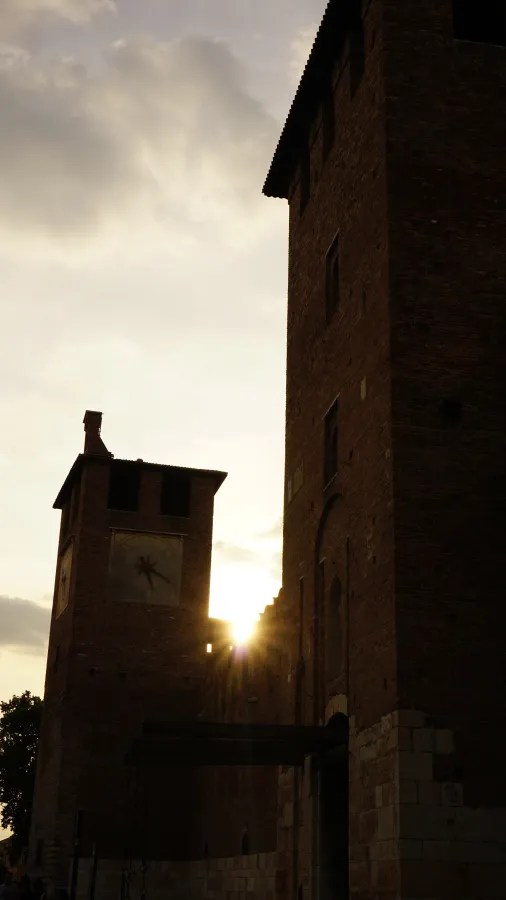 Silhouetted medieval brick towers against a cloudy sky with the sun peeking through