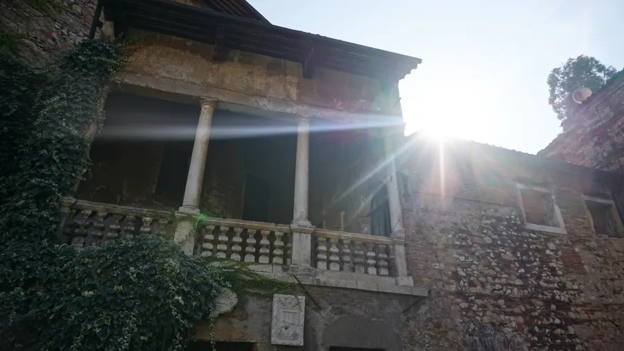 An old stone building with a balcony and climbing ivy in bright sunlight