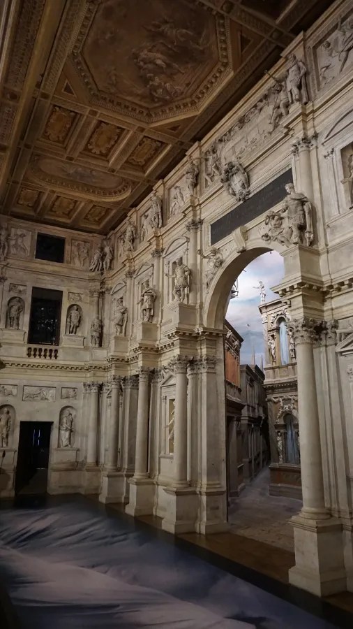 Ornate classical theater interior with numerous statues, coffered ceiling, and forced-perspective street scene.