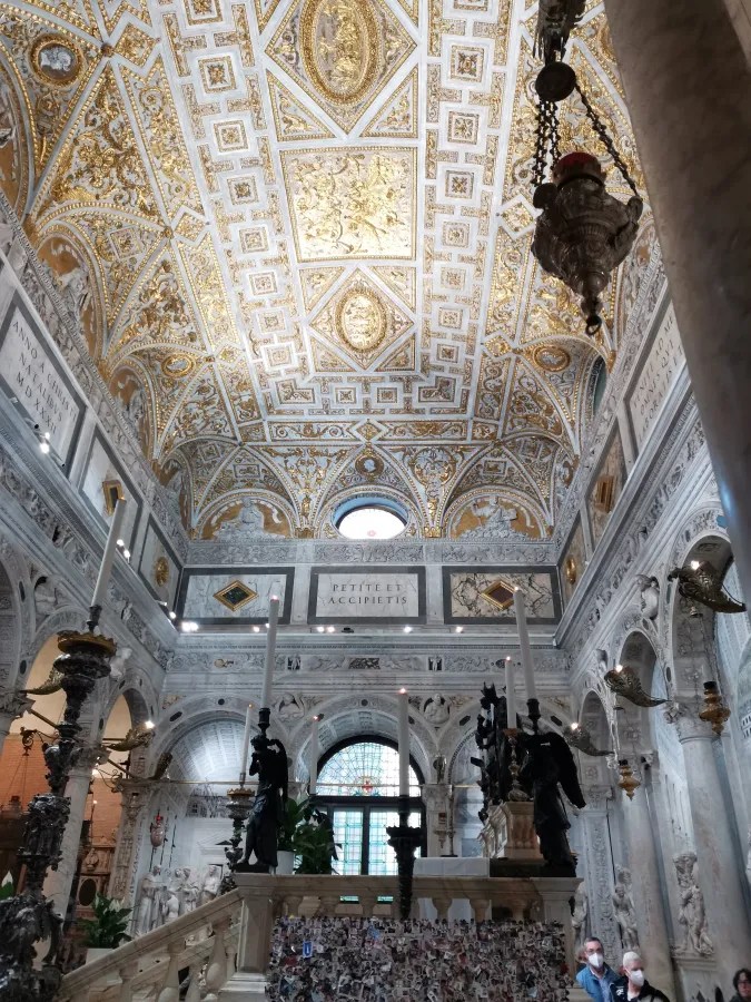 Ornate church interior with a gilded vaulted ceiling, large candles, and Latin inscriptions reading 'ANNO A CHRISTI NATALIBUS MDXXXII', 'PETITE ET ACCIPIETIS', and 'VENITE AD ME OMNES QUI LABORATIS'.