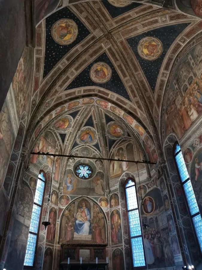 Interior of a chapel featuring vaulted ceilings and walls covered in narrative religious frescoes.