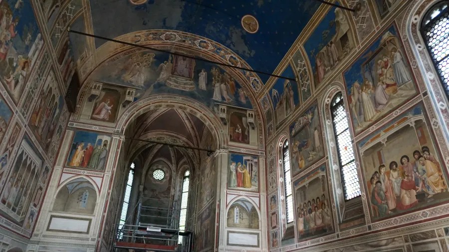 Interior of a chapel with intricate religious frescoes covering the walls and vaulted blue ceiling.
