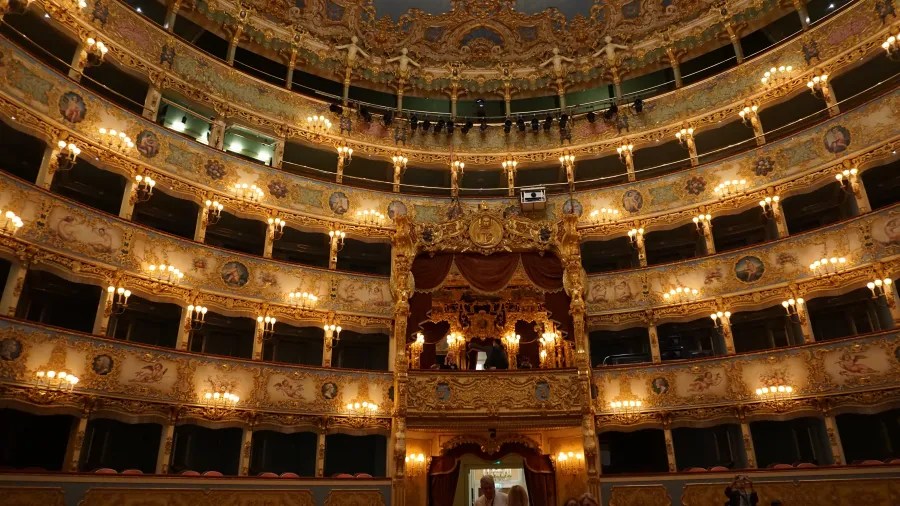 Ornate interior of a grand opera house with tiered, gold-decorated balconies.