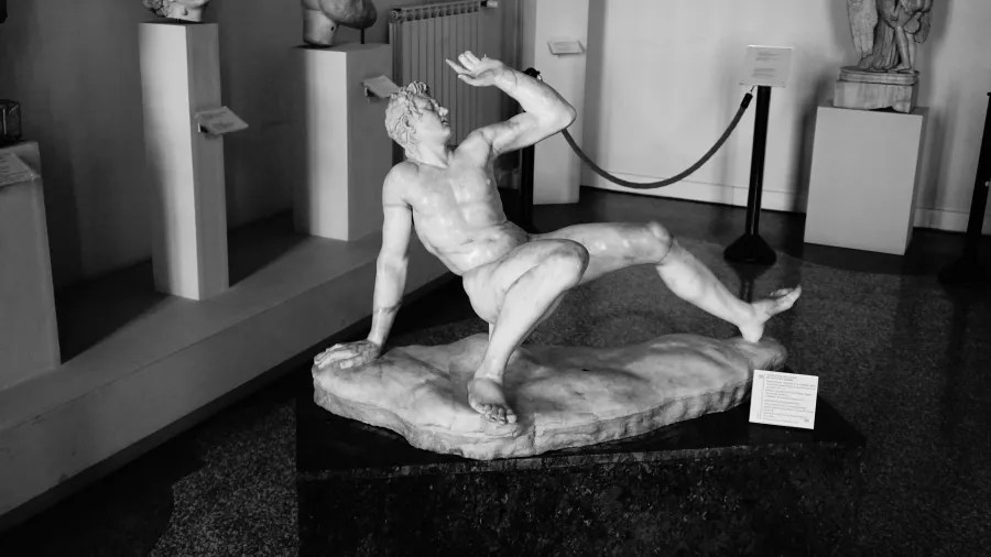 Marble statue of a reclining male figure shielding his face in a museum gallery