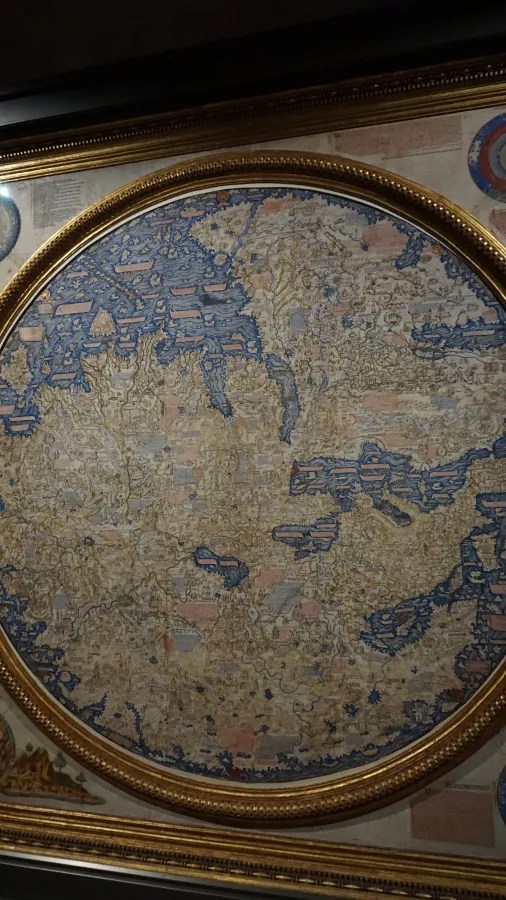 Detailed medieval circular world map with intricate geography and oceans within an ornate gold frame.