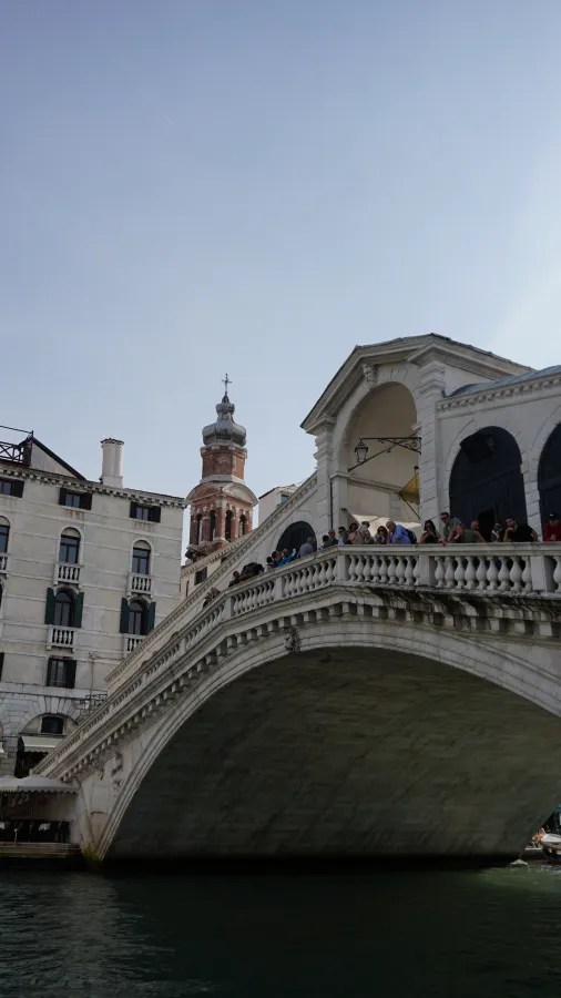 Low-angle view of the Rialto Bridge in Venice with tourists and a distant bell tower