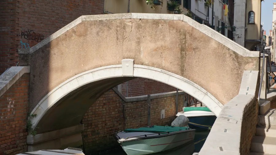 A small stone bridge over a canal in Venice with boats moored underneath.