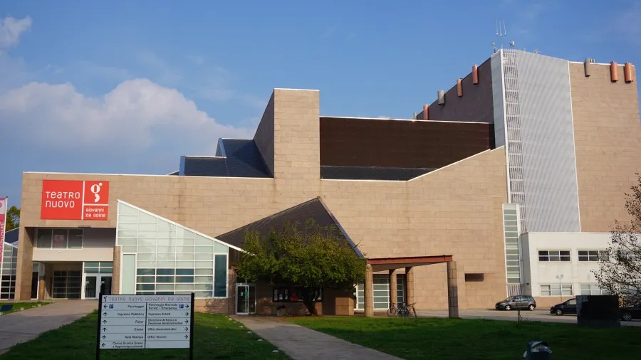 20221015_2_Italien_Udine (3) The exterior of Teatro Nuovo Giovanni da Udine, a modern multi-tiered building with a red sign.