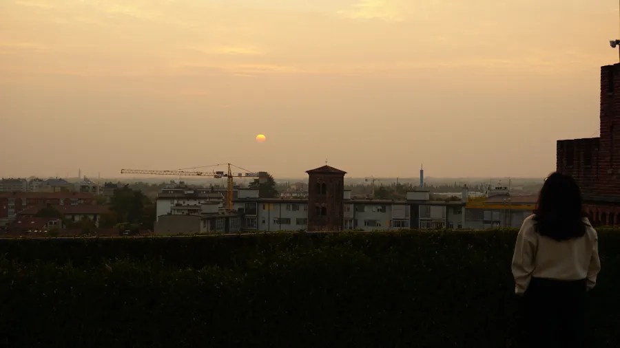 20221015_2_Italien_Udine (56) A person watching a sunset over a hazy city skyline with a construction crane.