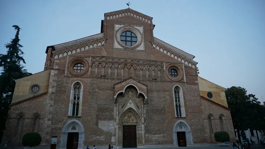 Historical Romanesque architecture of Udine Cathedral Brick facade of Udine Cathedral featuring a central rose window and arched decorative patterns.