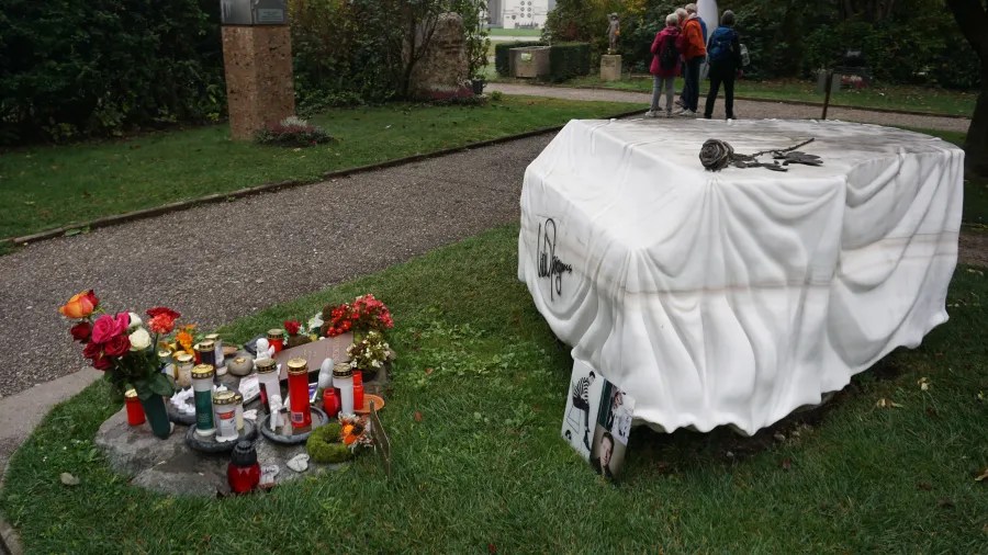 Udo Jürgens memorial grave featuring a white marble piano sculpture draped in cloth, flowers, and candles.
