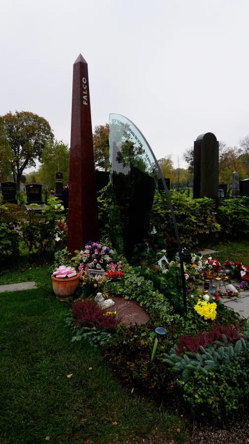 The grave of musician Falco featuring a tall red obelisk and a curved glass monument