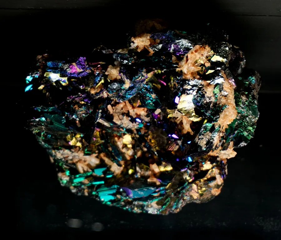 Iridescent crystalline mineral specimen with vibrant rainbow colors and small embedded tan crystals