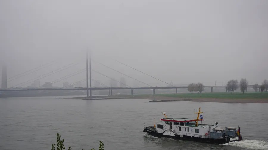Motorboat on a river with a large bridge partially hidden by thick fog.