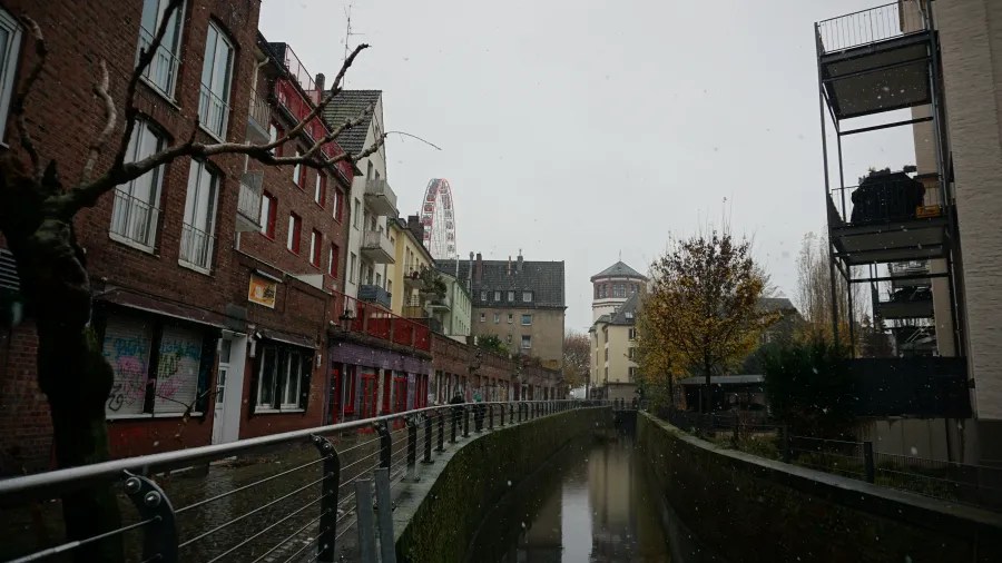 City canal lined with brick buildings under a grey sky with falling snow