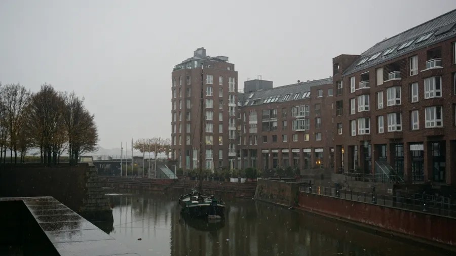 A canal with a boat and red brick buildings on a rainy, overcast day