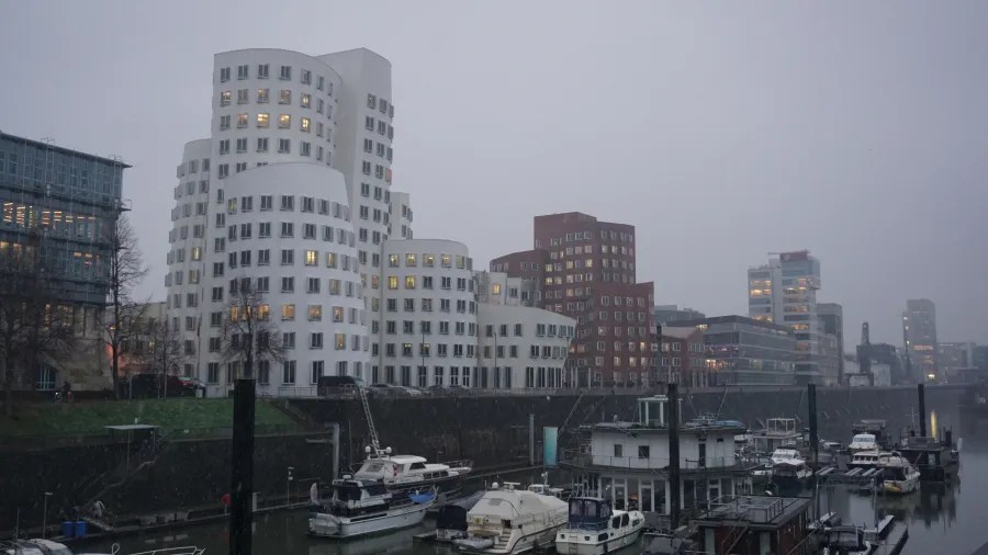 Modern curved white buildings and a red brick complex in a city harbor at dusk