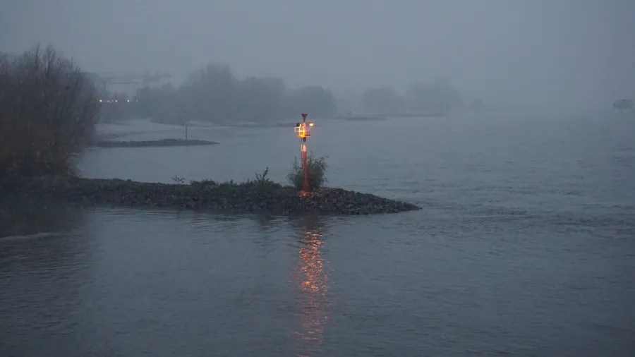 Orange navigation light on a rocky jetty in dense fog overlooking calm water