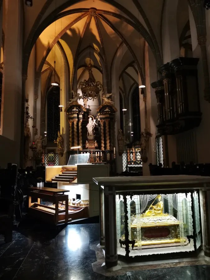 Interior of a church with an ornate altar, organ console, and lit golden reliquary.