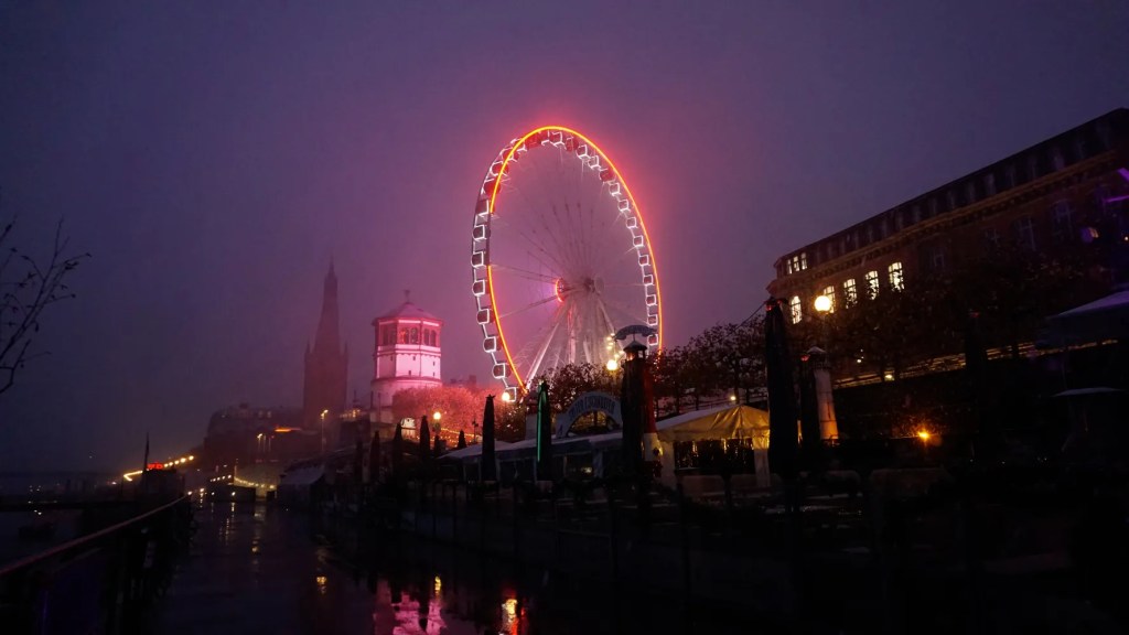 Glowing orange Ferris wheel on a misty night by a city waterfront.