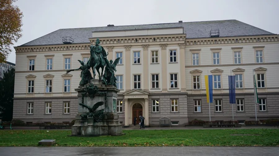 German Ministry of Justice building labeled JUSTIZMINISTERIUM with an equestrian statue in the foreground
