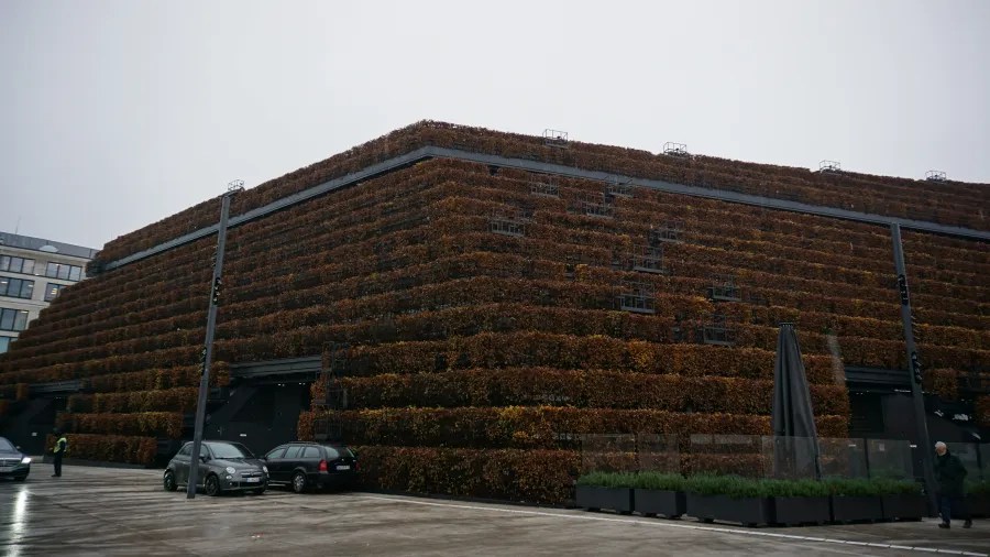 Large building with tiered facades entirely covered in brown hedges under a cloudy sky