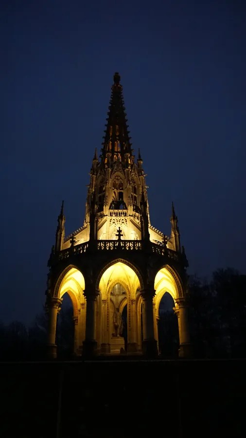 Illuminated Gothic monument at night with an intricate spire and glowing arched base.