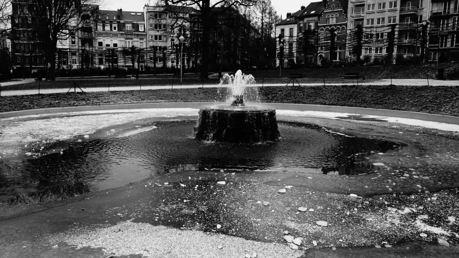 Black and white photograph of a central fountain in an urban park.