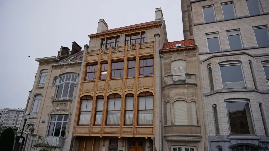 An Art Nouveau building with an intricate orange facade nestled between two traditional stone buildings.