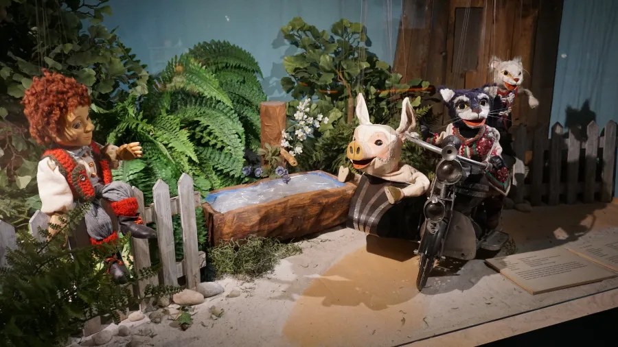 Puppets of a boy on a fence and animals on a motorcycle with a sidecar