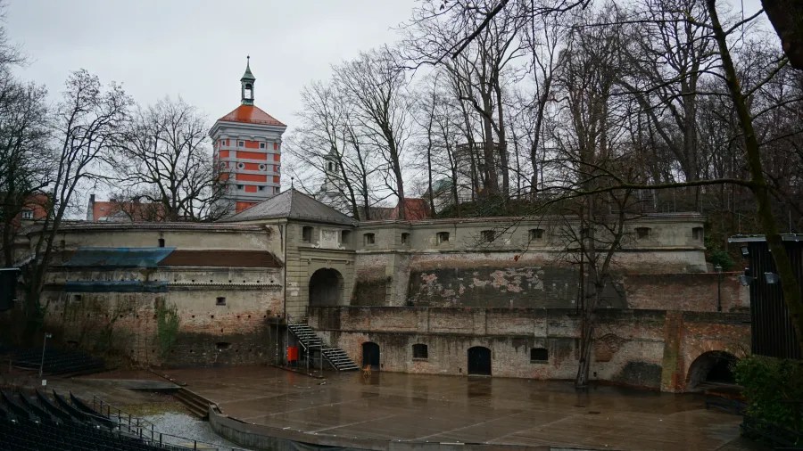 Historic stone city walls and gatehouse with a red and white tower in the background.
