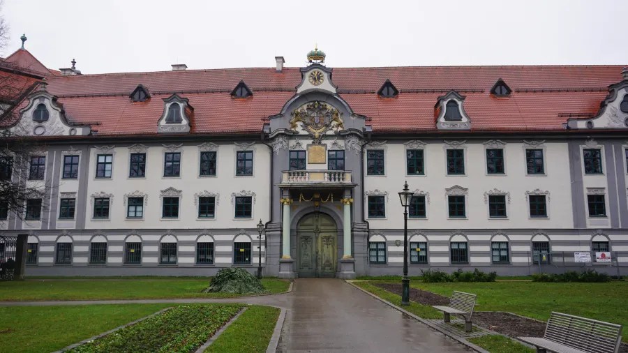 Facade of a grand, three-story historical building with a red tiled roof and central portal