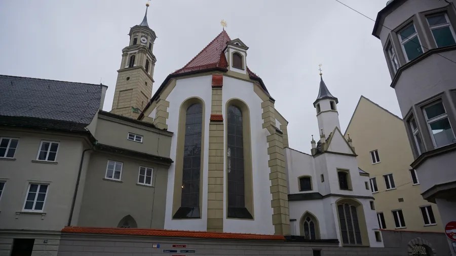 White church with tall arched windows and red-tiled roof beside a clock tower