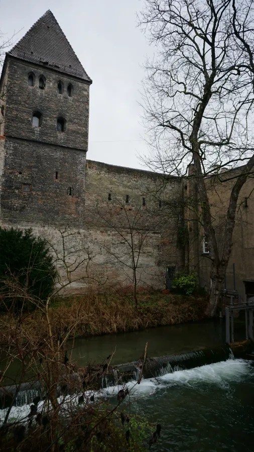 Medieval stone tower and defensive wall beside a canal with a small weir.