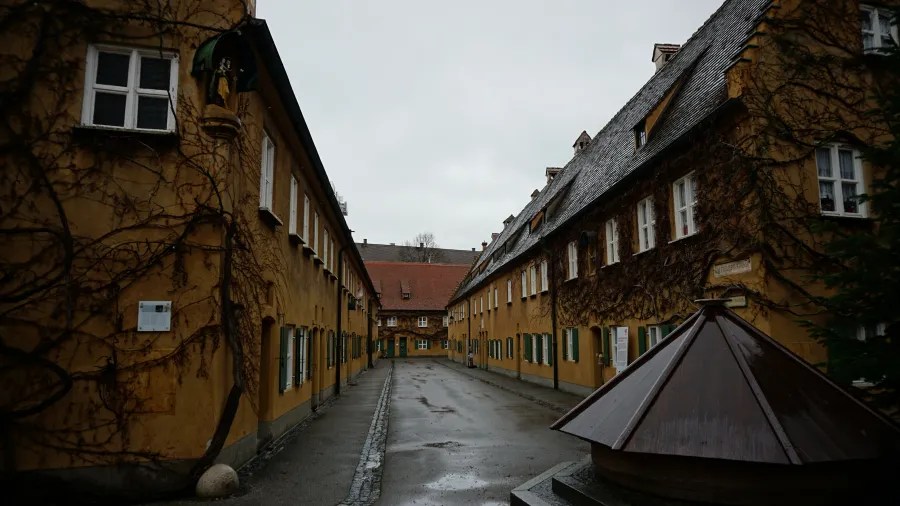 Narrow alleyway lined with historic yellow terraced houses featuring green shutters and climbing vines.