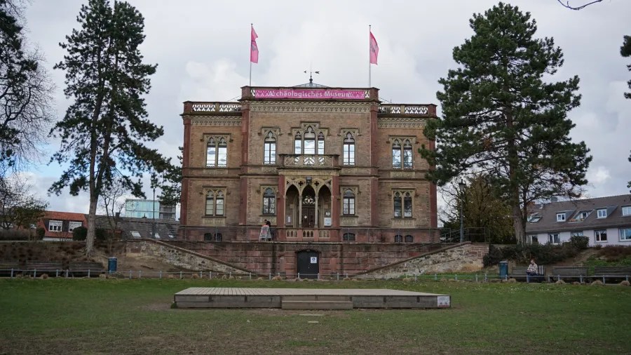 The Archäologisches Museum building with pink flags and a small wooden stage in front.