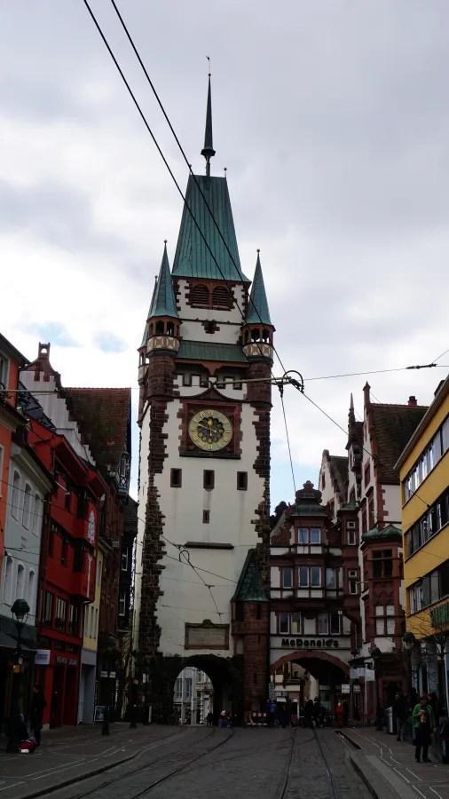 Medieval Martinstor gate tower with a clock face and spire above a city street.