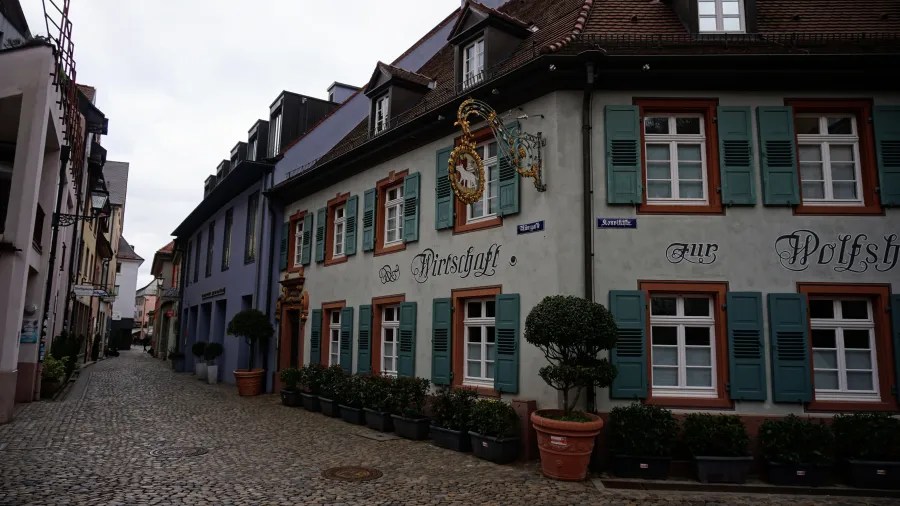 Narrow cobblestone street in an old town with a historic building labeled 'Wirtschaft Zur Wolfsh'.