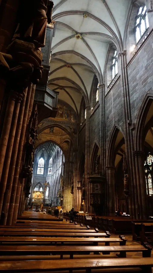 Gothic cathedral interior with high vaulted ceilings, stone arches, and rows of wooden pews