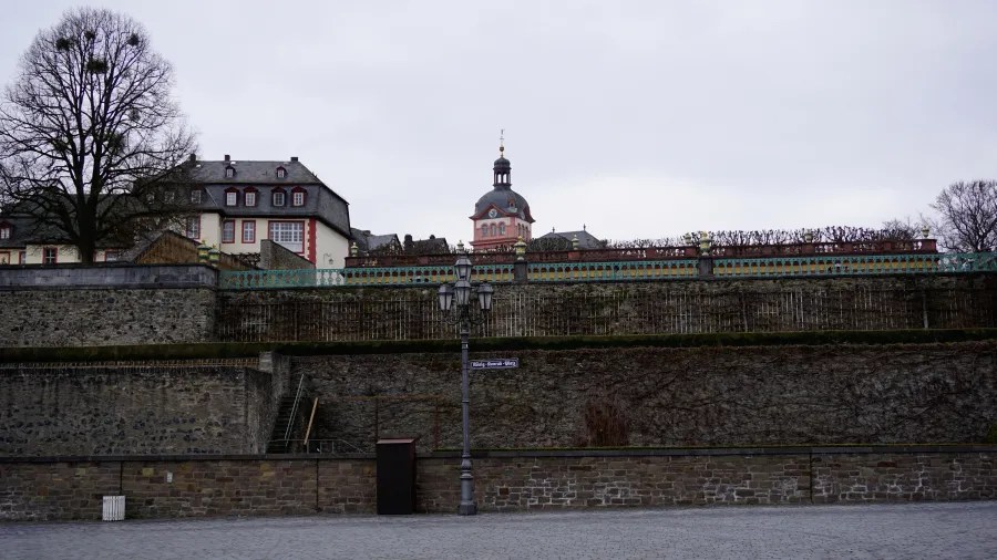 Historical terraced stone walls lead up to traditional buildings and a domed clock tower under an overcast sky.