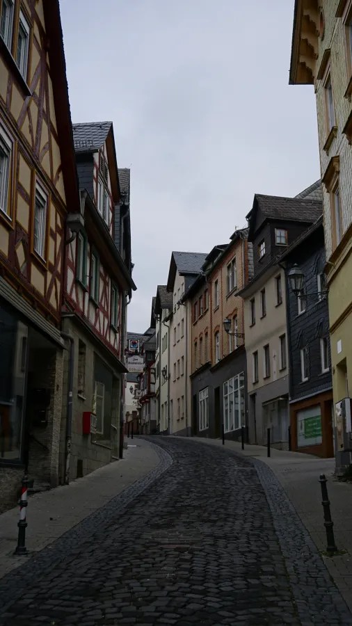 Narrow cobblestone street winding through a European town with historic half-timbered buildings.