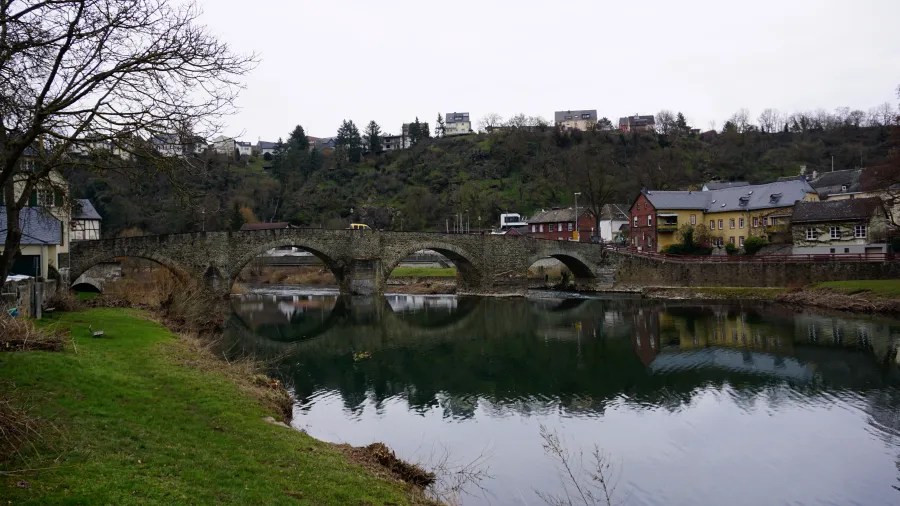 Historic stone arch bridge over a river reflecting houses and a hillside town.
