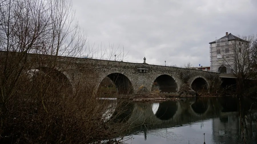 A multi-arched stone bridge crossing a river, with a tall building at one end.