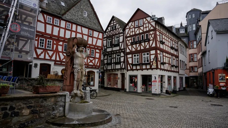 Cobblestone town square featuring historic half-timbered houses and a stone statue fountain.