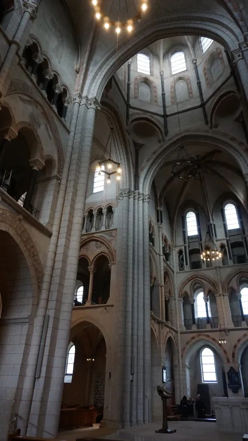 Interior of a grand stone cathedral featuring soaring vaulted ceilings, arched galleries, and chandeliers