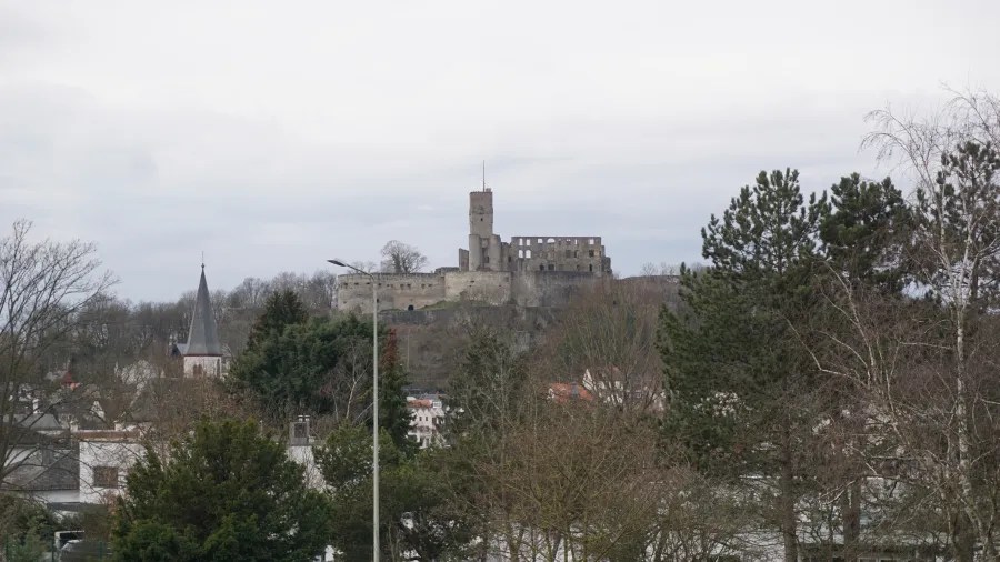 20230319_Deutschland_Hessen_3-Burgen-Weg (13) Stone castle ruins on a hilltop overlooking a town with a church spire
