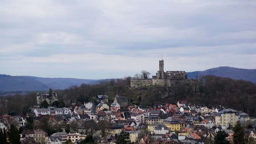 20230319_Deutschland_Hessen_3-Burgen-Weg (17) Overview of a town with red-roofed buildings and a large stone castle on a hill.